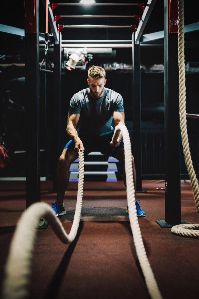 fit man working out with battle ropes at fitness gym