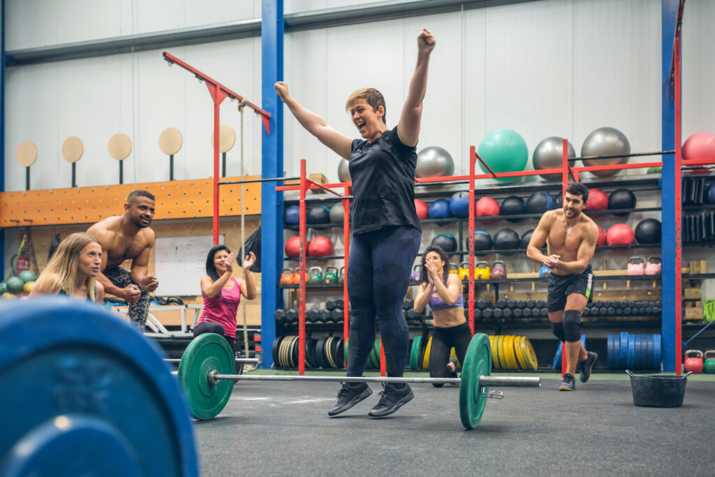 happy woman celebrating her weightlifting achievement while her gym mates cheering her on
