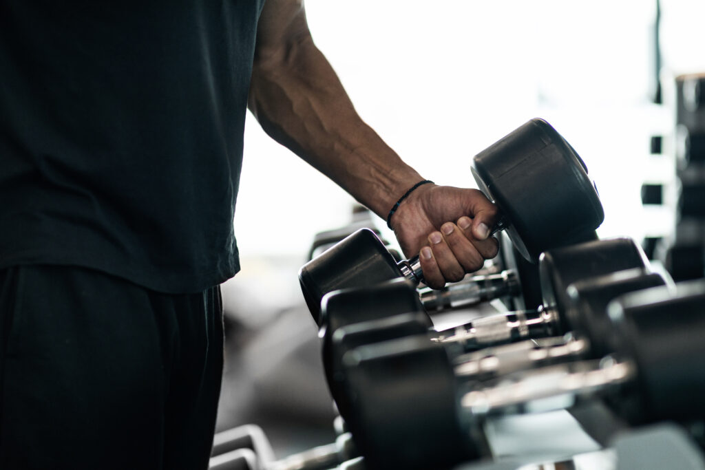 sport equipment. unrecognizable black male athlete taking dumbbell from rack at gym