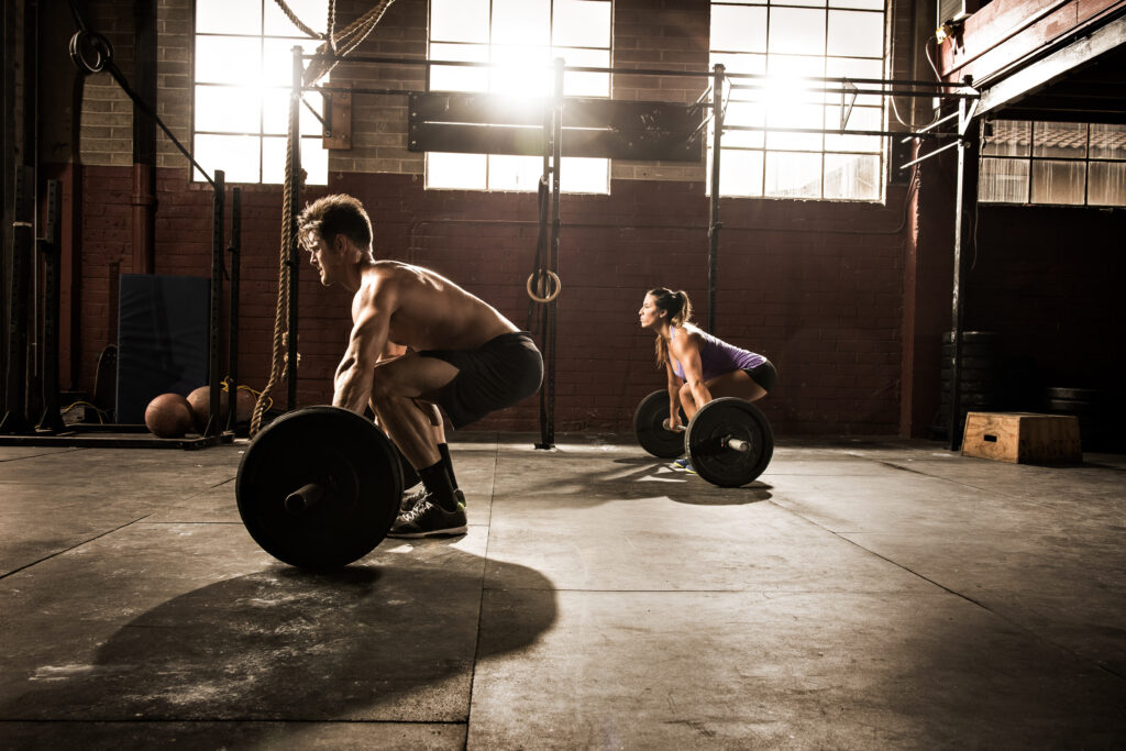 two young adults working out with barbells in gym